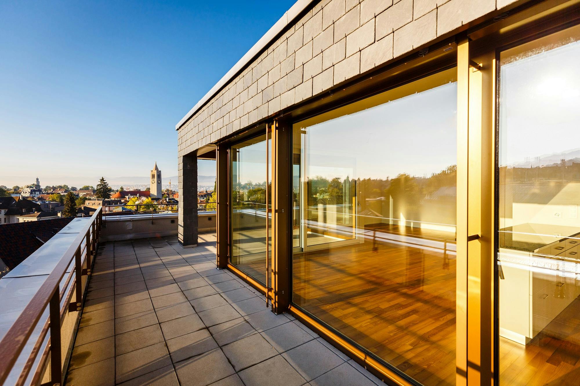 Moderne Terrasse mit Glasfront und Blick auf die Stadt bei Sonnenuntergang.