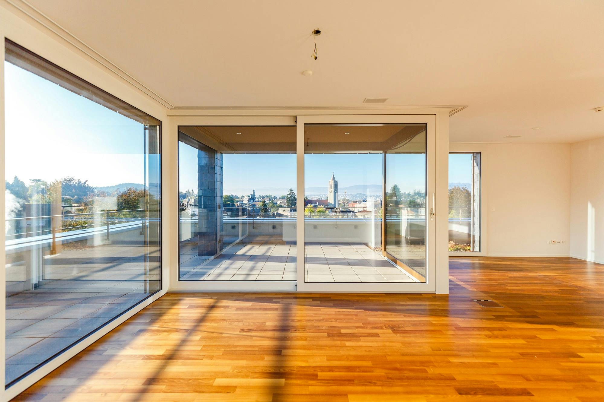Helles, modernes Wohnzimmer mit Parkettboden und Glas-Schiebetür zur Terrasse mit Stadtblick.